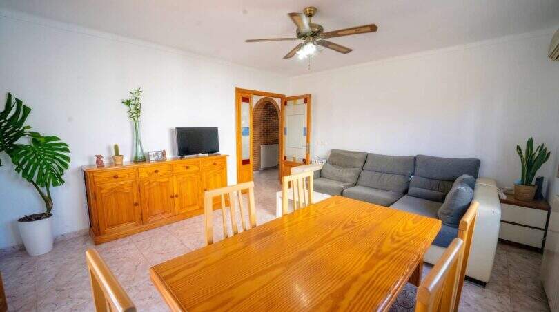 Helles Wohn-Esszimmer mit Holztisch, grauem Sofa, Deckenventilator und Bogendurchgang in Einfamilienhaus Porto Colom