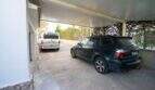 Überdachter Carport mit zwei Fahrzeugen beim Einfamilienhaus in Porto Colom, umgeben von Grünflächen.
