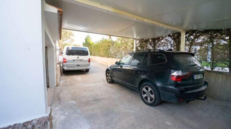 Überdachter Carport mit zwei Fahrzeugen beim Einfamilienhaus in Porto Colom, umgeben von Grünflächen.