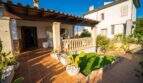 Überdachte Terrasse mit Terrakottafliesen, Steinsäulen, Kakteen und gepflegtem Rasen eines Einfamilienhauses in Porto Colom.