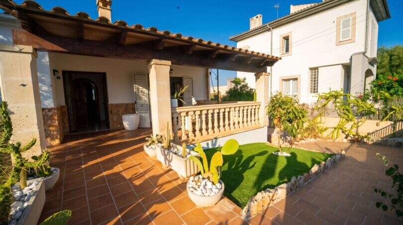 Überdachte Terrasse mit Terrakottafliesen, Steinsäulen, Kakteen und gepflegtem Rasen eines Einfamilienhauses in Porto Colom.