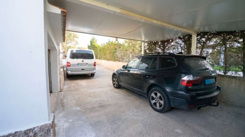 Cochera cubierta con dos plazas de aparcamiento en la casa unifamiliar en Porto Colom, rodeada de áreas verdes.