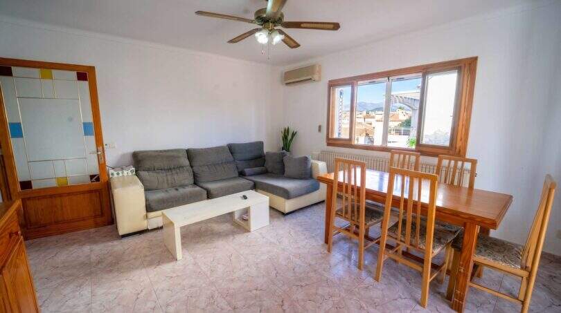 Helles Wohnzimmer mit grauem Sofa, Holzesstisch, Deckenventilator und Klimaanlage in Haus Porto Colom