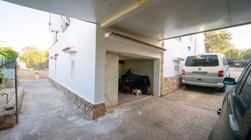 Cochera con puerta de garaje abierta, fachada blanca y piedra natural en la casa unifamiliar en Porto Colom.