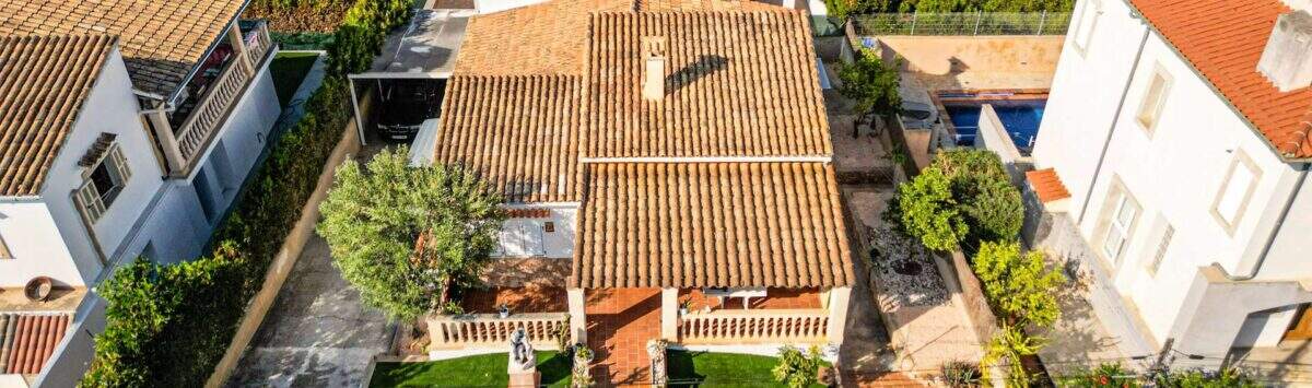 Luftaufnahme eines charmanten Einfamilienhauses in Porto Colom mit Terrakottadach, gepflegtem Garten und Pool.