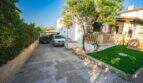 Einfahrt mit Carport und zwei Fahrzeugen, gepflegter Rasen und mediterrane Terrasse eines Einfamilienhauses in Porto Colom.