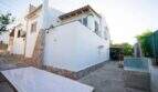 Außenansicht Einfamilienhaus Porto Colom: weißer Natursteinbau mit Carport, Terrassentisch und mediterranem Flair.