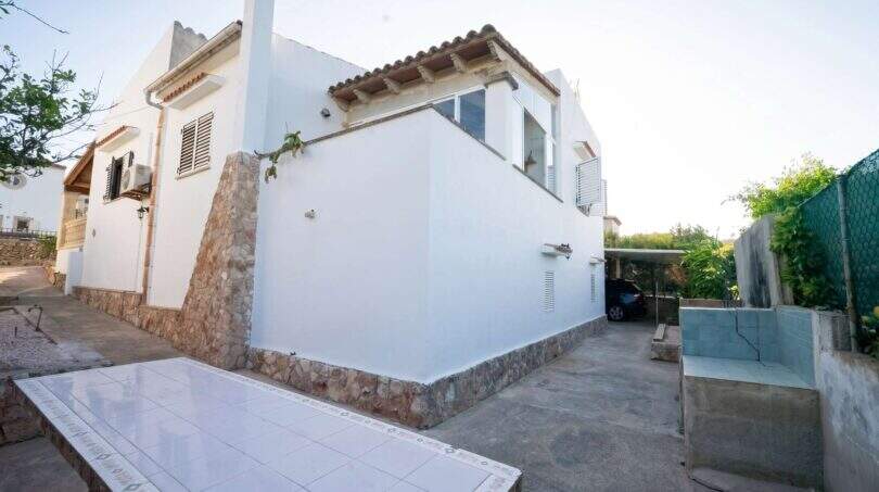 Außenansicht Einfamilienhaus Porto Colom: weißer Natursteinbau mit Carport, Terrassentisch und mediterranem Flair.