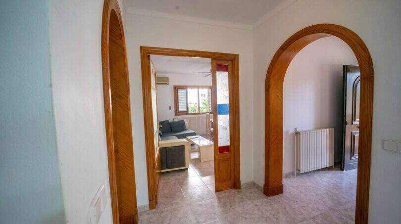 Heller Flur mit eleganten Rundbögen aus Holz, Marmorfliesen und Blick ins Wohnzimmer des Hauses in Porto Colom.