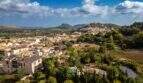 Luftaufnahme von Capdepera mit historischer Burganlage, mediterraner Bebauung, Grünflächen und Bergpanorama im Hintergrund.