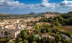 Aerial view of Capdepera with historic castle complex, Mediterranean architecture, green spaces and mountain panorama in the background.