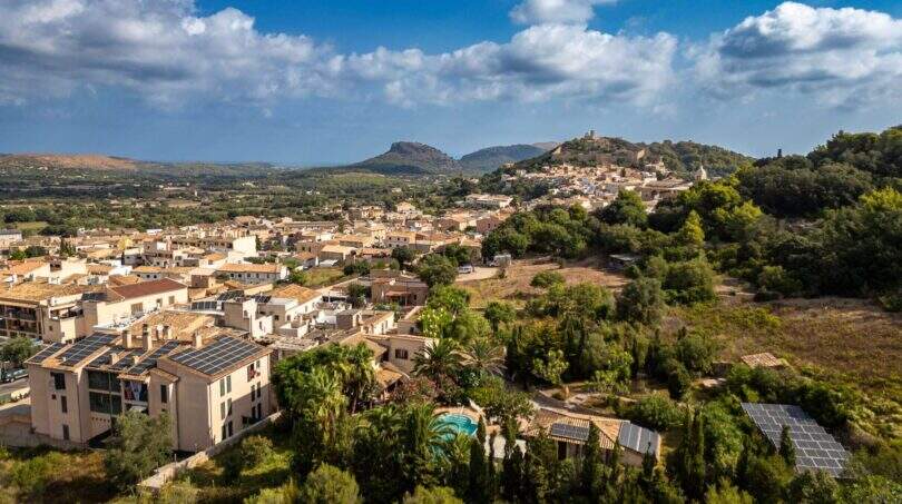Luftaufnahme von Capdepera mit historischer Burganlage, mediterraner Bebauung, Grünflächen und Bergpanorama im Hintergrund.