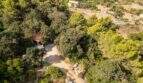 Luftaufnahme eines bewaldeten Grundstücks in Capdepera mit kleinem Gebäude, Schotterweg und üppiger mediterraner Vegetation.