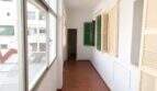 Langer Flur mit Terrakottaboden, Glasfront und grünen Fensterläden in renovierungsbedürftiger Wohnung in Palma
