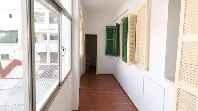 Langer Flur mit Terrakottaboden, Glasfront und grünen Fensterläden in renovierungsbedürftiger Wohnung in Palma
