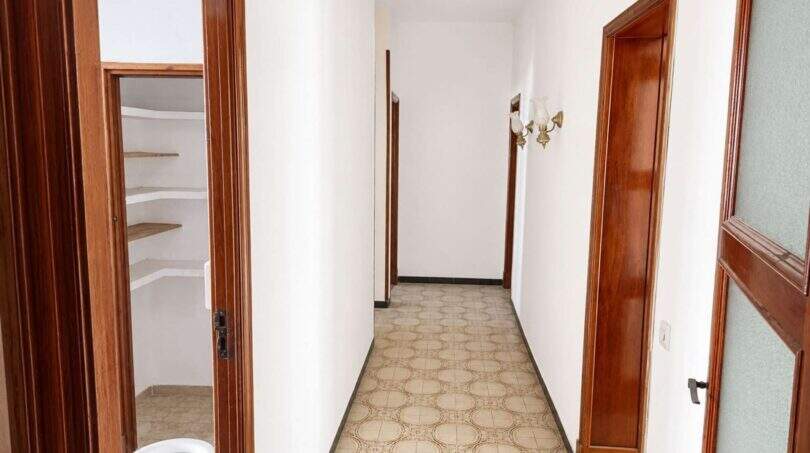 Langer Flur mit gemustertem Fliesenboden, Holztüren und Wandleuchte in renovierungsbedürftiger Wohnung in Palma