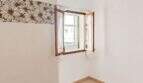 Leeres Zimmer mit geöffnetem Holzfenster, weißen Wänden und Blumentapetenbordüre in Wohnung Palma