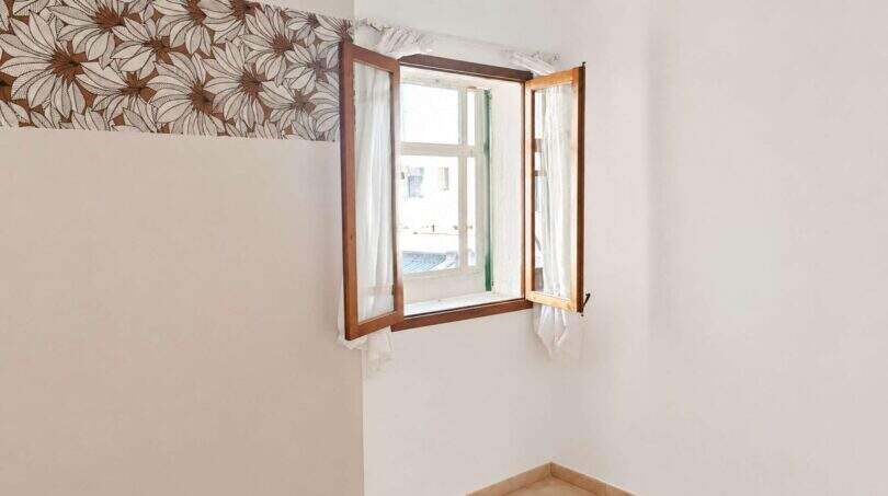 Leeres Zimmer mit geöffnetem Holzfenster, weißen Wänden und Blumentapetenbordüre in Wohnung Palma