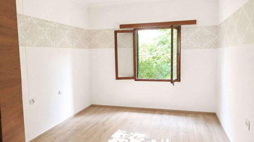Leerer Wohnraum mit Holzparkett, Tapetenbordüre und geöffnetem Holzfenster mit Gartenblick in Palma
