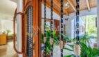 Eingangsbereich einer mediterranen Villa in Sa Coma mit Holztür, Natursteinboden und tropischen Pflanzen.
