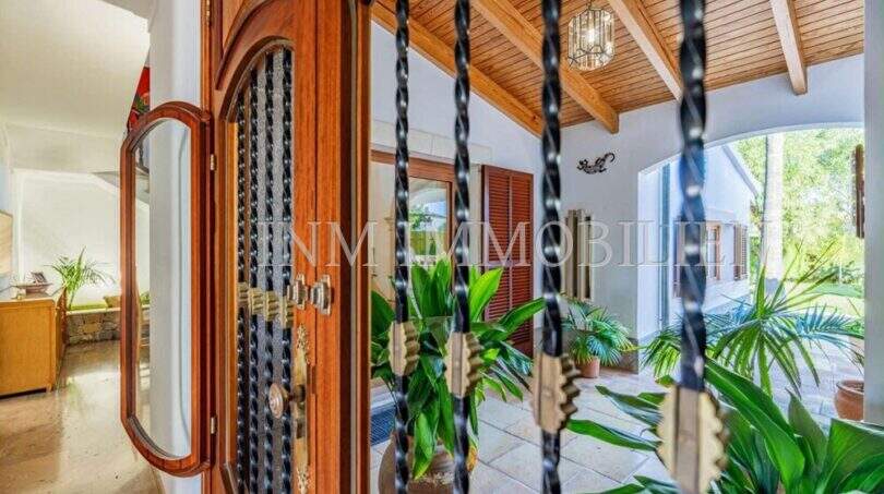 Eingangsbereich einer mediterranen Villa in Sa Coma mit Holztür, Natursteinboden und tropischen Pflanzen.