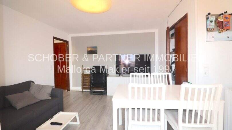 Helles Wohnzimmer mit grauem Sofa, weißem Esstisch und TV in modernisierter Wohnung in Cala Ratjada