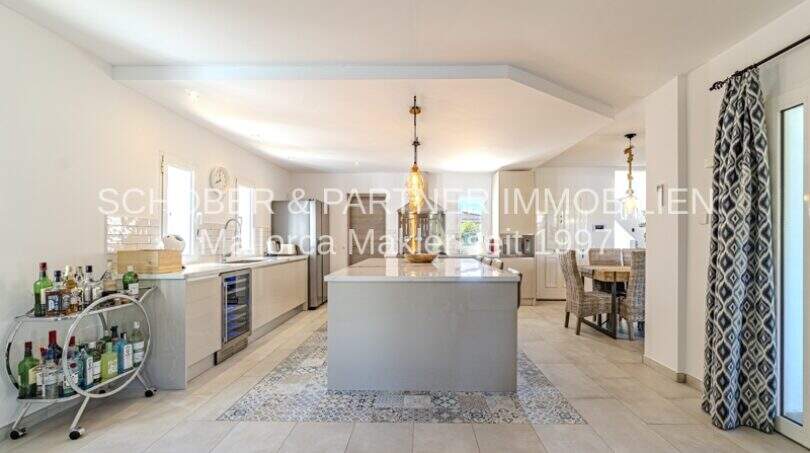 Moderne offene Küche mit Kochinsel, Hängelampen und Barwagen in mediterraner Villa, Sa Coma