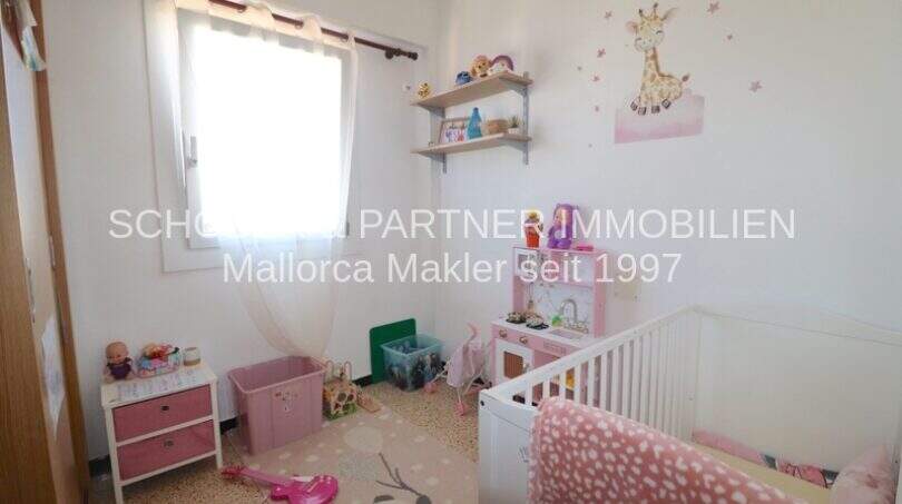 Habitación infantil con cuna blanca, juguetes, decoración rosa y pegatina de jirafa en la pared en apartamento cerca del mar, Porto Cristo