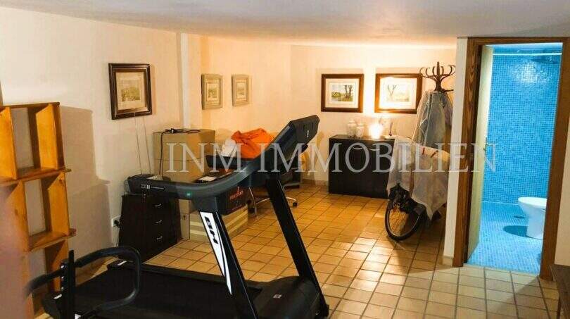 Fitnessraum mit Laufband und angrenzendem Bad mit blauen Mosaikfliesen im rustikalen Haus in S'Aranjassa