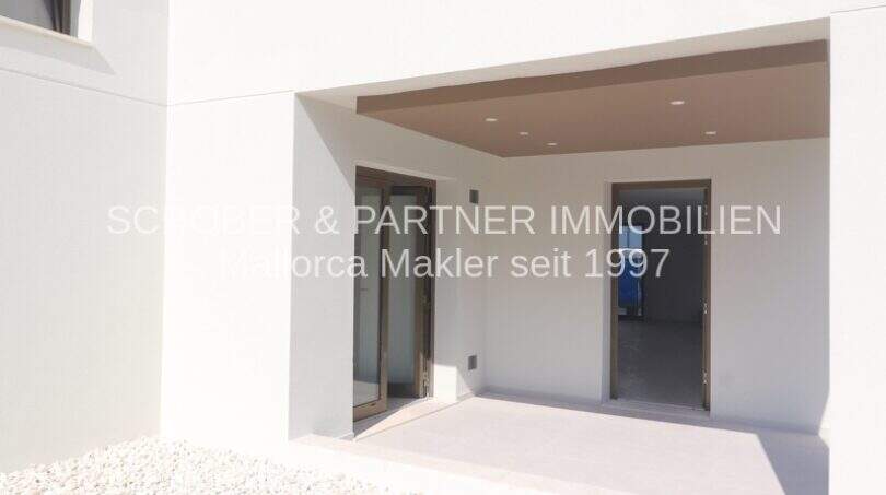 Área de entrada cubierta de un apartamento moderno de nueva construcción en Cala Millor con puerta de vidrio y focos