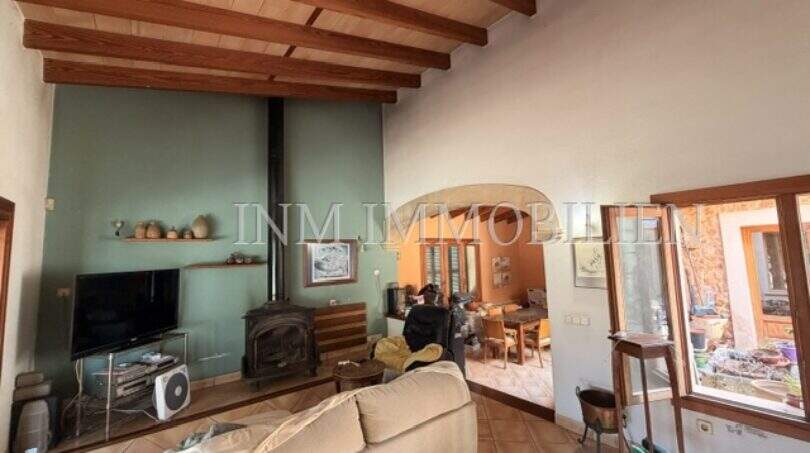 Wohnzimmer der Finca in Llucmajor mit Holzbalkendecke, Kaminofen, Sofa und Blick ins Esszimmer.