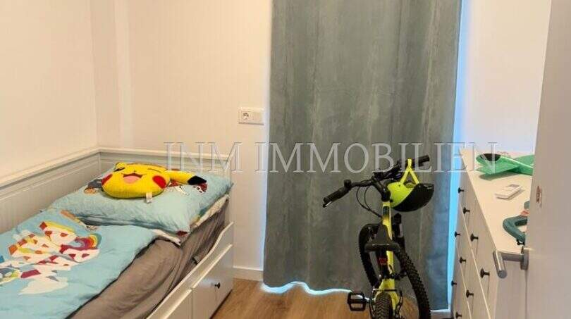 Kinderzimmer der Wohnung in Cala d'Or mit Einzelbett, Fahrrad und Kommode auf Holzboden.