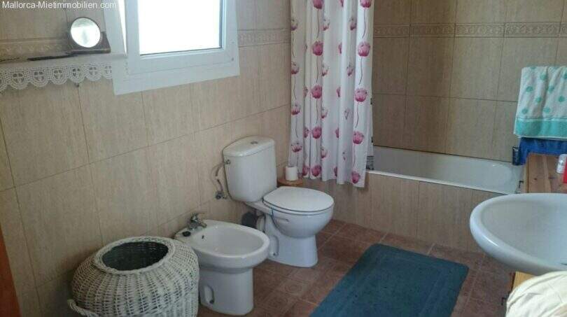 Tiled bathroom with bathtub, shower curtain, toilet, bidet and sink in the Cala Murada chalet