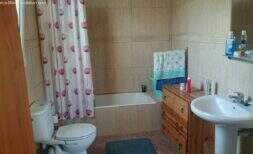Baño del chalet en Cala Murada con bañera, inodoro, lavabo y cómoda de madera, paredes de azulejos claros
