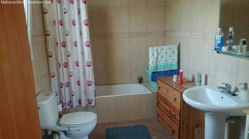 Bathroom of the chalet in Cala Murada with bathtub, toilet, sink and wooden dresser, bright tiled walls