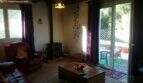 Living room with leather sofa, fireplace stove, purple curtains and glass door to the sunny terrace with garden view.