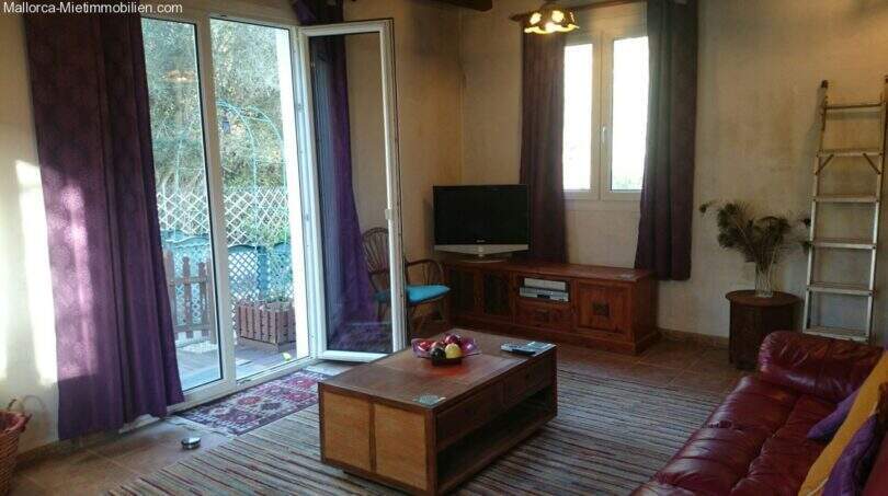 Living room of the chalet in Cala Murada with leather sofa, wooden furniture, purple curtains and terrace access to the forest.