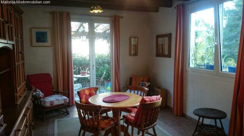 Bright dining room in the Cala Murada chalet with wooden table, red curtains and terrace door to the garden with forest view.
