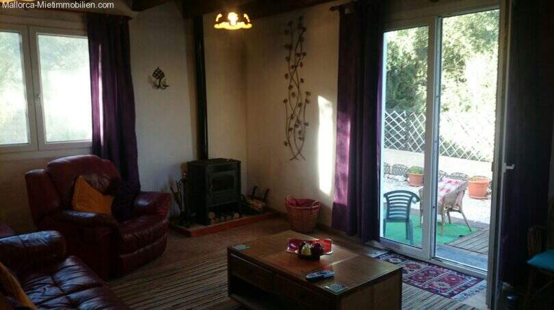 Living room with leather sofa, wood stove and purple curtains, terrace access to the fenced garden of the chalet