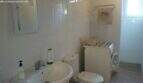 Bright bathroom of the Cala Murada chalet with sink, toilet, mirror and washing machine, white tiled.