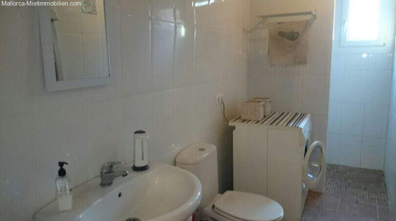 Bright bathroom of the Cala Murada chalet with sink, toilet, mirror and washing machine, white tiled.