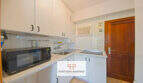 Helle Küche mit weißen Schränken, Mikrowelle, Einbauherd und Holztür im Apartment in Cales de Mallorca