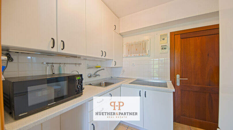 Helle Küche mit weißen Schränken, Mikrowelle, Einbauherd und Holztür im Apartment in Cales de Mallorca