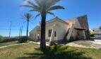 Mediterrane Villa in Cala Murada mit Palmen, Steinverkleidung, Balustrade und gepflegtem Rasen bei strahlendem Sonnenschein.