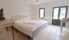 Helles Schlafzimmer im sanierten Landhaus mit Doppelbett auf Rollen, Natursteinboden und Terrassentür zum Garten