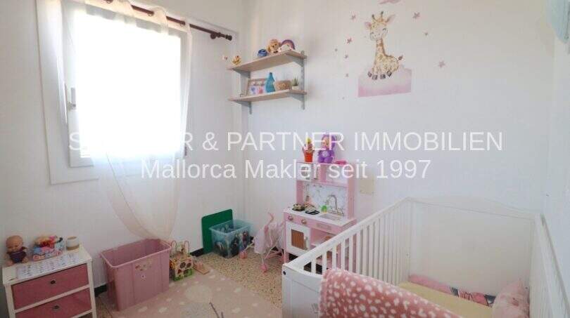 Habitación infantil con cuna, juguetes, decoración de pared con jirafa y ventana en apartamento Porto Cristo