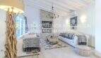Helles Wohnzimmer der mediterranen Villa in Sa Coma mit weißen Holzbalken, Kaminwand und eleganter Ausstattung.