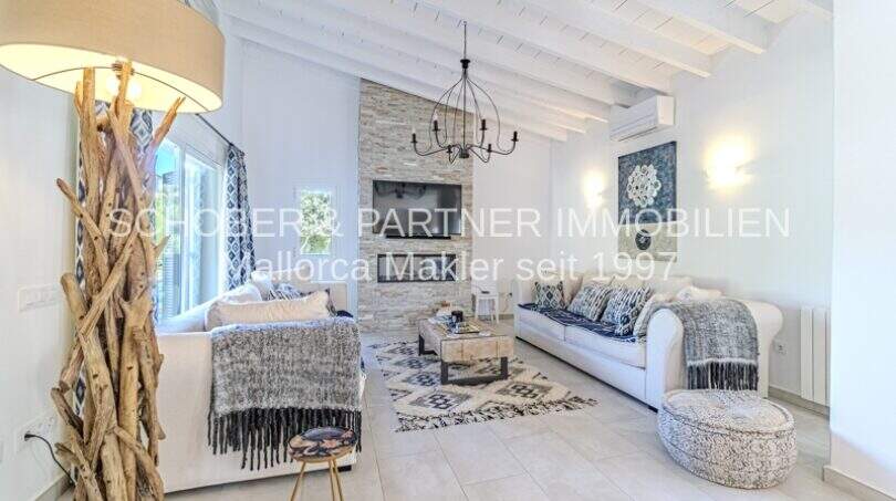 Helles Wohnzimmer der mediterranen Villa in Sa Coma mit weißen Holzbalken, Kaminwand und eleganter Ausstattung.