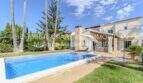 Mediterrane Villa in Sa Coma mit blauem Pool, Palmen und gepflegtem Garten unter sonnigem Himmel.