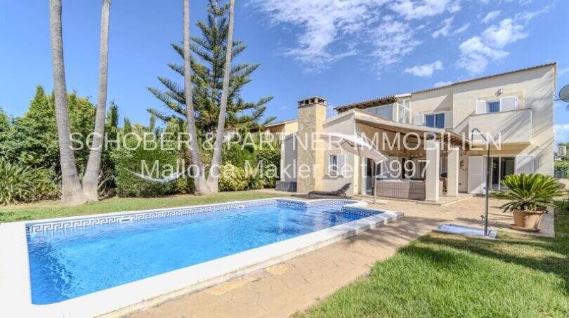 Mediterrane Villa in Sa Coma mit blauem Pool, Palmen und gepflegtem Garten unter sonnigem Himmel.